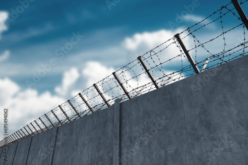 Concrete wall with barbed wire against blue sky. Concept border, prisons, refugees, loneliness. mixed media, copy space. photo