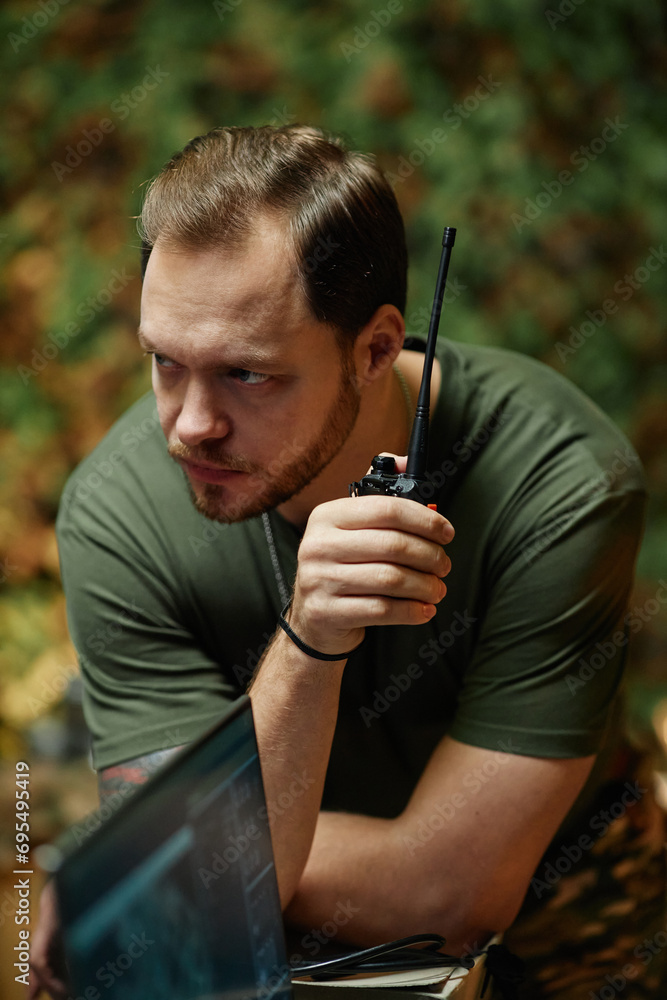 Young serious male officer speaking to portable radio transmitter and looking at surveillance camera on computer screen Young serious male officer speaking to portable radio transmitter and looking at surveillance camera on computer screen