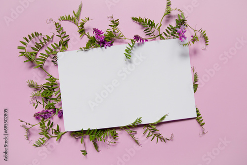 White paper invitation on a composition of colorful flowers. Place for text