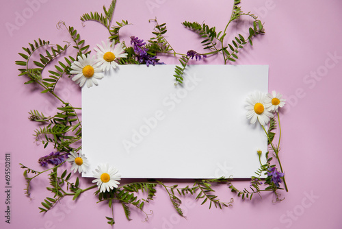 White paper card note laying in bright flowers bouquet. Romantic wedding invitation. Present for women. Space for text. Place for text