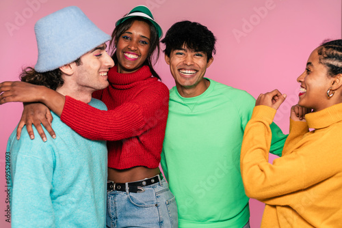 Group of four friends in vivid sweaters smiling together with a pink background photo