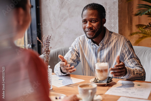 Young African American businessman explaining something to female colleague while enjoying lunch break in cozy cafe photo
