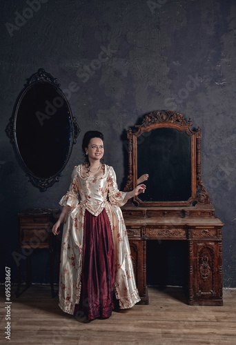 Beautiful woman in rococo style medieval dress standing near console mirror table