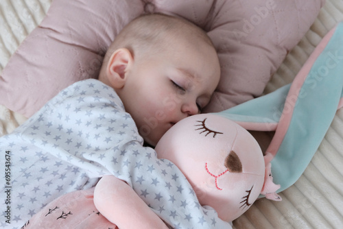 Baby with pink bunny soft toy. A girl of European appearance, wearing a light light jumpsuit, is sleeping in the crib. Sleep mode, care and hygiene.