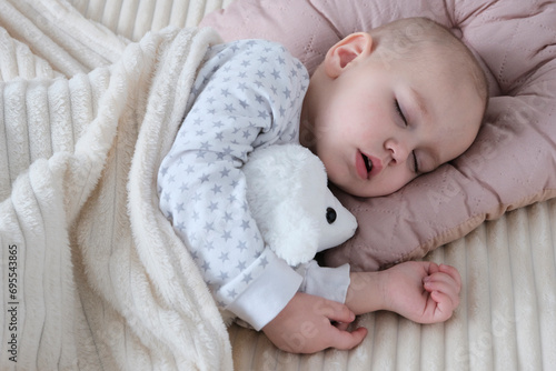 A cute baby, a child, a girl of European appearance, in a light light jumpsuit, is sleeping in the crib. Soft toy, ram, in hands. Sleep mode, care and hygiene.