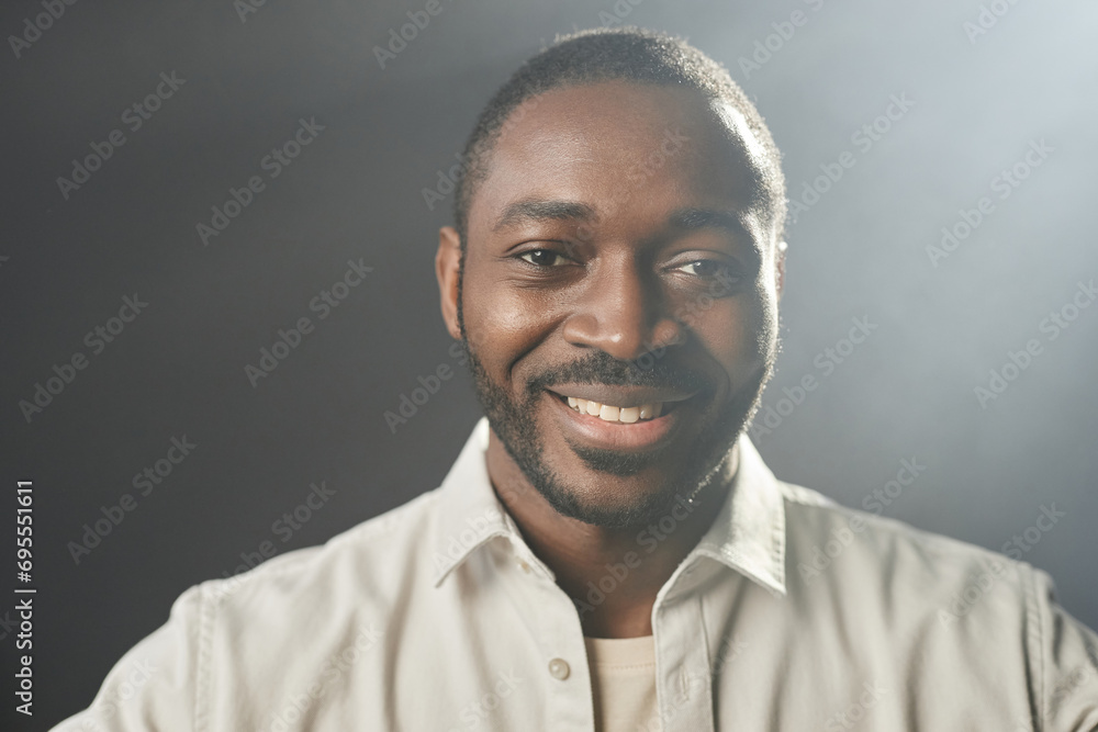 Fototapeta premium Front view portrait of smiling adult African American man looking at camera with side lighting