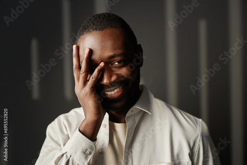 Front view portrait of carefree Black man smiling at camera with hand covering face