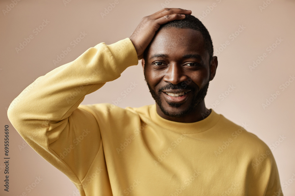 Minimal portrait of adult Black man looking at camera in studio with hand on hair Minimal portrait of adult Black man looking at camera in studio with hand on hair