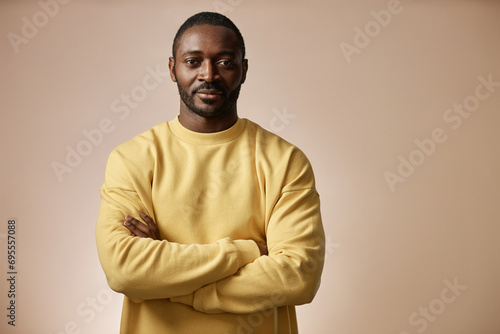 Minimal portrait of confident Black man looking at camera in studio standing with arms crossed against neutral background, copy space photo