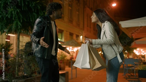 Ethnic Arabian Indian angry aggressive couple with shopping bags quarrel woman slap on cheek man hit on face throw purchases go away boyfriend and girlfriend conflict misunderstanding in evening city photo