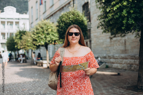 Portrait beautiful woman in sunglasses with paper map in street. Happy tourist travels in Europe. Vacation concept by exploring interesting places to travel. Women Searching locations at summer day. © mdyn