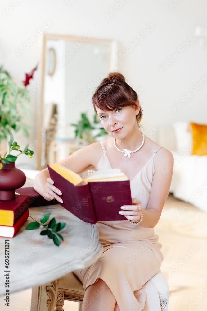 Adult woman reading a book at home, sitting in classic light living room Adult woman reading a book at home, sitting in classic light living room