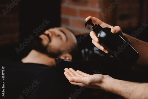 Mockup dark shampoo bottle on background of man in barbershop washing hair. Concept spa cosmetic for head men