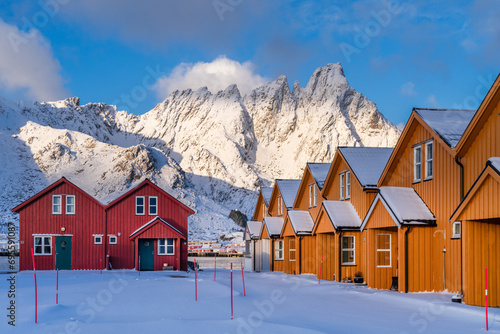 View of typical Lofoten wooden houses with snow capped mountains and sunlight