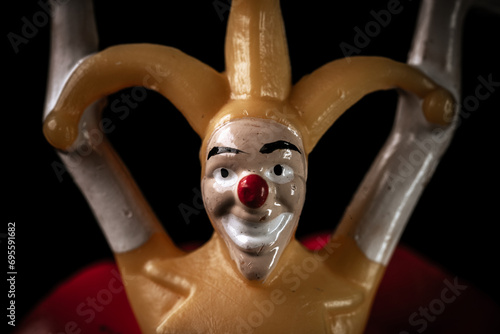 Creepy dirty toy jester in the dark. Scary face of a jester with a red nose on a black background