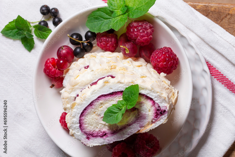 Meringue roll with whipped cream and currant curd, served with berries on a ceramic plate. Rustic style.