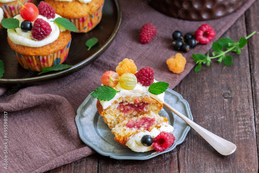 Cupcakes with butter cream and raspberry curd, decorated with berries on a wooden surface.