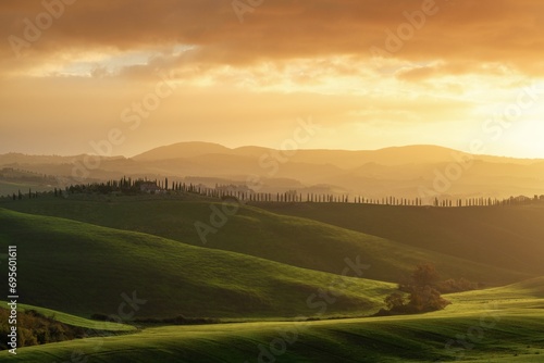 warm sunrise landscape in the rolling hills of Tuscany with green fields and trees