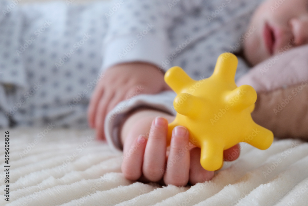 A baby is sleeping in a crib, a child of European appearance, wearing a light light jumpsuit. A yellow rubber toy in the hand. Sleep patterns for babies, care and hygiene. A baby is sleeping in a crib, a child of European appearance, wearing a light light jumpsuit. A yellow rubber toy in the hand. Sleep patterns for babies, care and hygiene.
