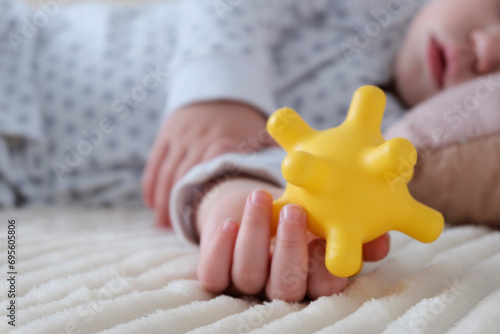 A baby is sleeping in a crib, a child of European appearance, wearing a light light jumpsuit. A yellow rubber toy in the hand. Sleep patterns for babies, care and hygiene.