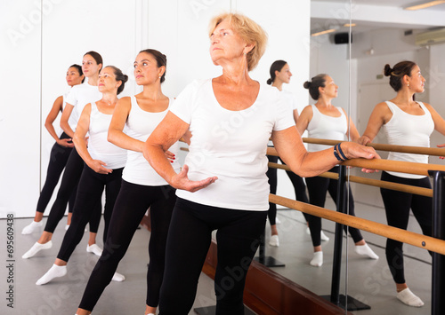 Group of women engaged in classical ballet in a dance studio perform the battement tendu movement, standing in a ballet ..stance near the barre