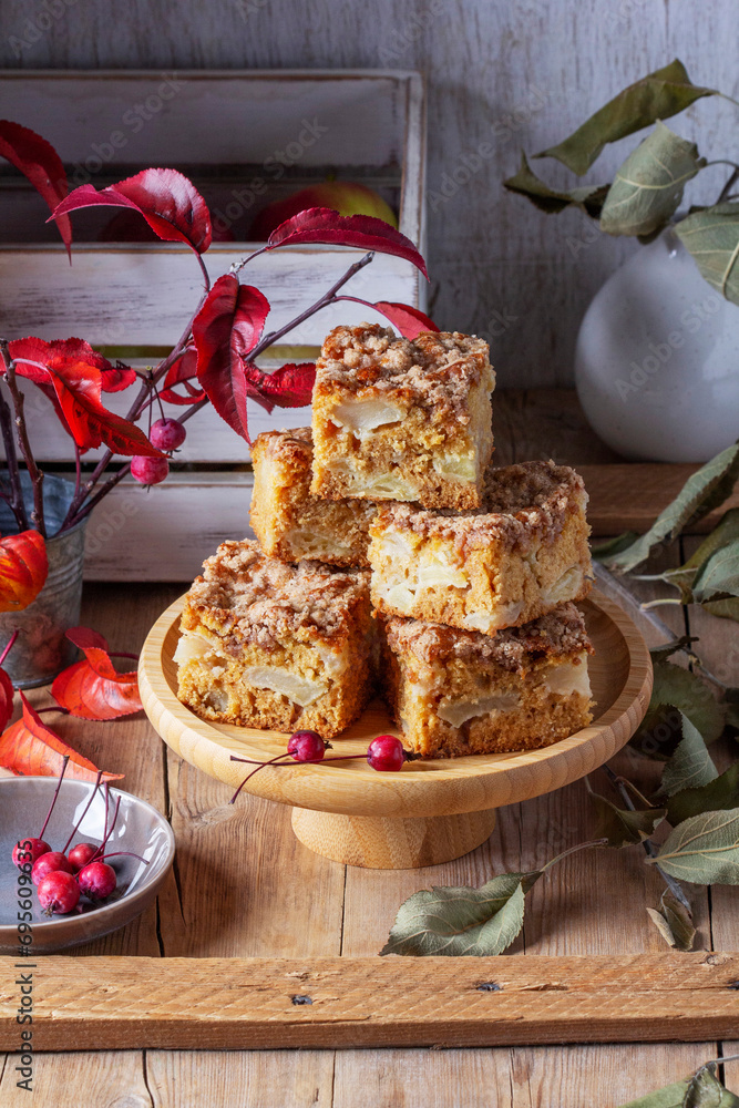Slices of Dutch apple cake with streusel on a wooden tray, apples and apple branches on a wooden background.