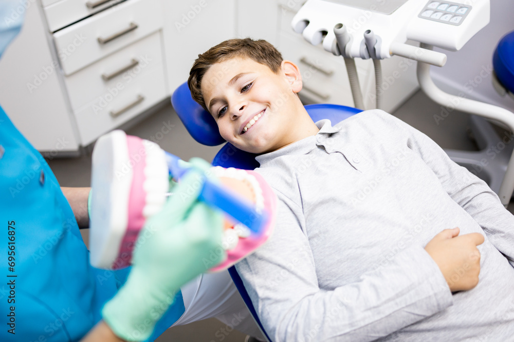 Obraz premium Teach kids how to brush their teeth! An unrecognizable dentist is teaching oral hygiene lessons to a child with a toy set of teeth. Use the toothbrush properly.