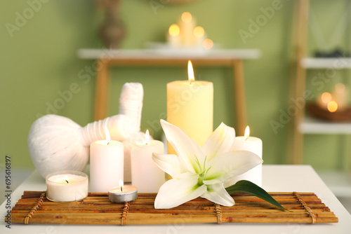 Burning candles with flower and herbal bags on table in spa salon  closeup