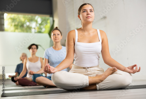 Young beautiful woman having yoga class sitting in lotus pose in sports yoga studio