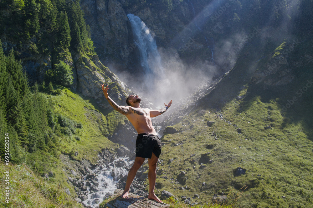 Obraz premium Man in Alps waterfall. Sexy man. Man freedom lifestyle. Meditating in nature. Hispanic man practicing yoga. Lifestyle relaxation concept, summer meditation on nature. Calmness and relax in nature.