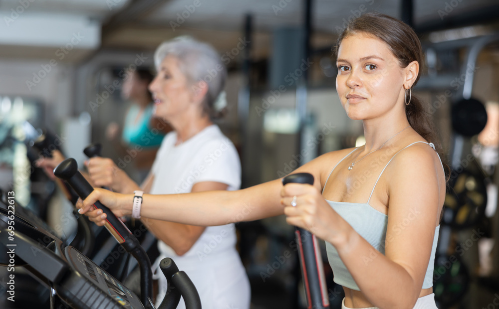Young athletic woman working out on elliptical machine in gym