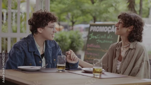 Duas mulheres sentadas à mesa de um restaurante ao ar livre, conversando e de maos dadas. Cinematico 4k. photo
