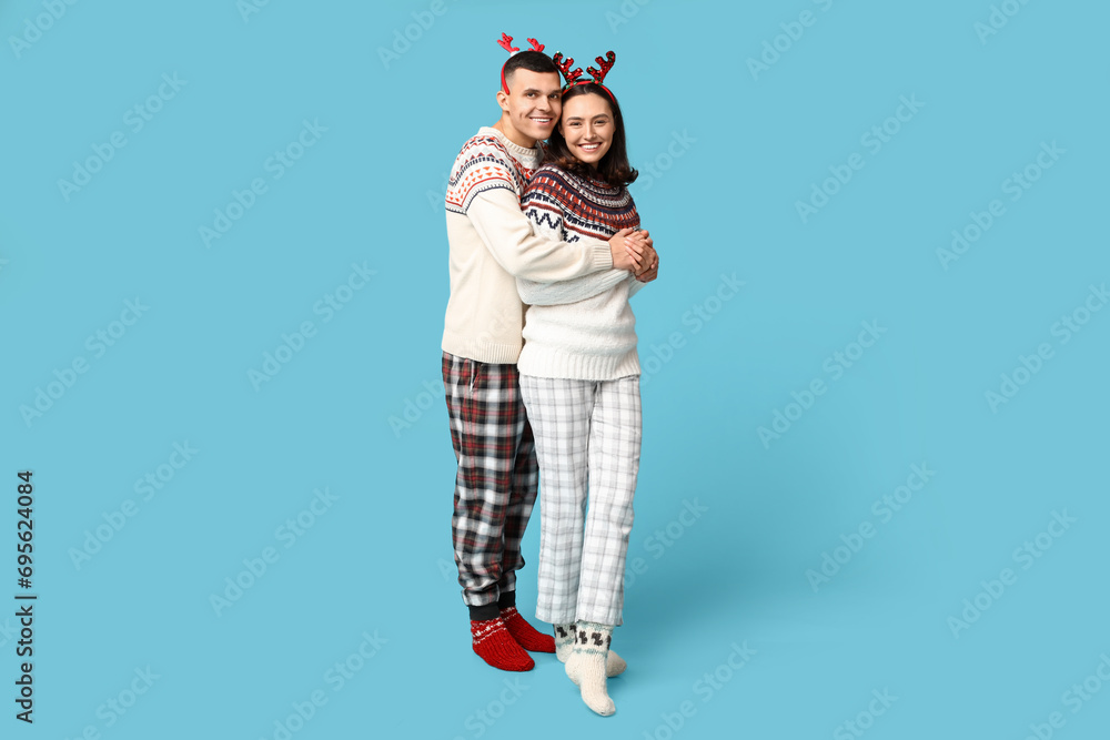 Fototapeta premium Happy young couple in Christmas pajamas hugging on blue background