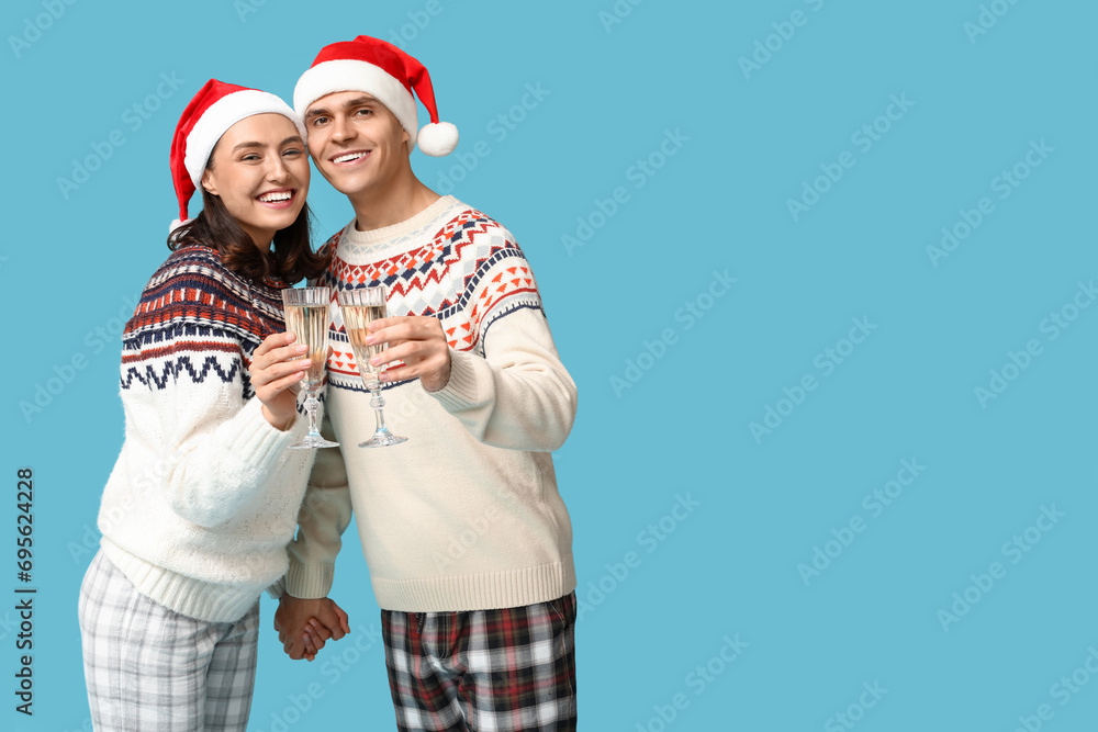 Happy young couple in Christmas pajamas and with champagne on blue background Happy young couple in Christmas pajamas and with champagne on blue background