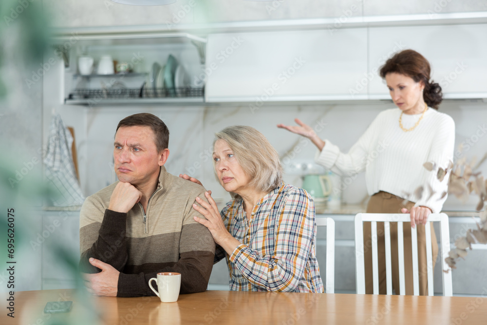 Obraz premium Family members quarreling in the kitchen and old woman trying to calm angry man sitting at the table
