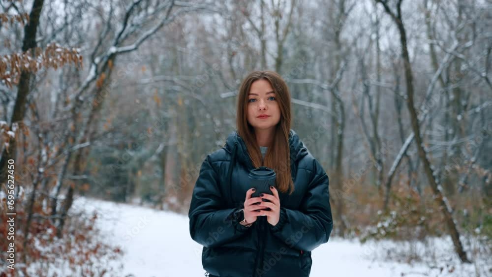 Woman in black jacket standing outdoors in winter with coffee cup in hands. Brunette puts on her hood and takes a sip of coffee while walking. Woman in black jacket standing outdoors in winter with coffee cup in hands. Brunette puts on her hood and takes a sip of coffee while walking.