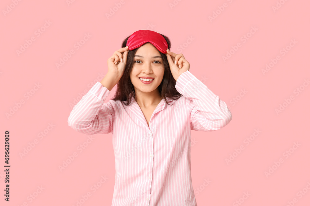 Beautiful young happy Asian woman in pajamas with sleeping mask on pink background Beautiful young happy Asian woman in pajamas with sleeping mask on pink background