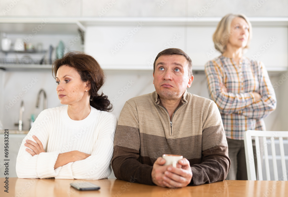 Angry middle-aged man and woman sitting at table and upset old woman ...