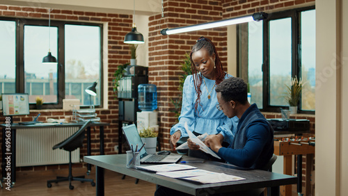 African american people planning report with annual data on papers and laptop, using online statistics to plan business development. Man and woman reviewing startup results in boardroom.