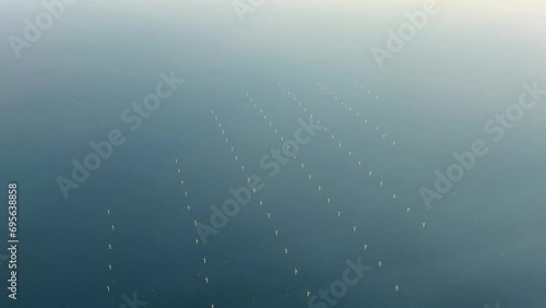 Aerial view of offshore wind farm with wind turbines on the North Sea, the Netherlands, Europe. Several large white and yellow wind turbines, wind mills on a blue, calm, sea. High quality Stock 4K photo