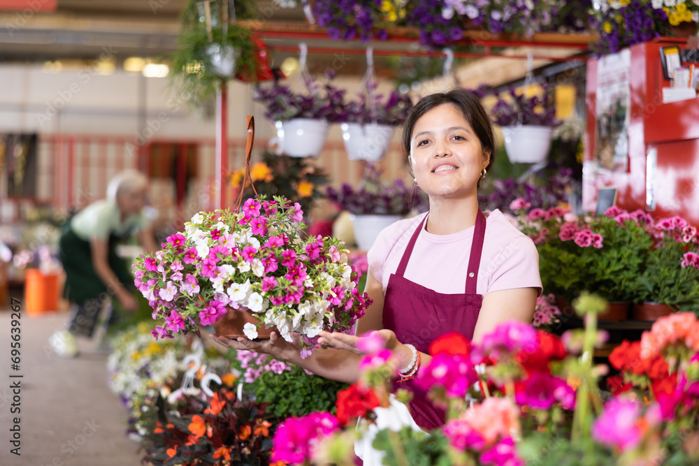 Glad middle-aged woman marketer demonstrating calibrachoa in garden pots in point of sale of plants