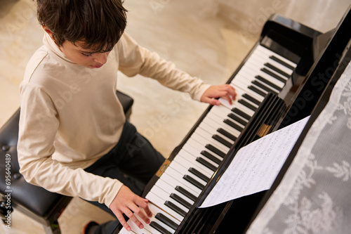 Multi ethnic teenage boy pianist creates music, touches the keys, performs on the pianoforte, composes a melody at home
