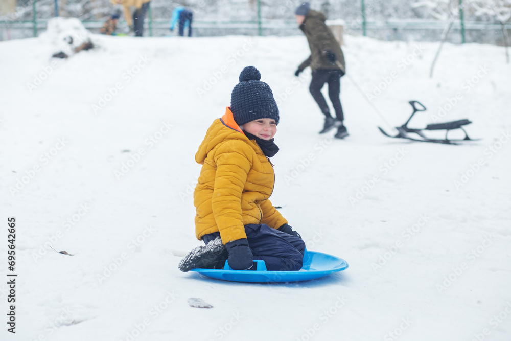 Child boy ride in snow plate. Outdoor play. Cold temperature. Winter time