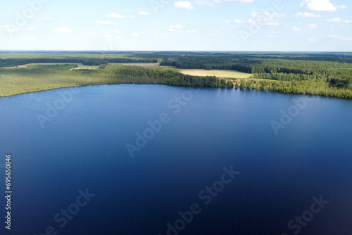 This aerial capture presents a vast, tranquil lake surrounded by a lush forest, creating a serene and expansive natural panorama
