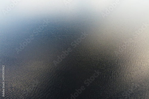 Aerial Expanse of Rippling Waters. The vastness of a serene lake is captured in this aerial photo, with gentle ripples on the water's surface creating a mesmerizing texture that invites contemplation