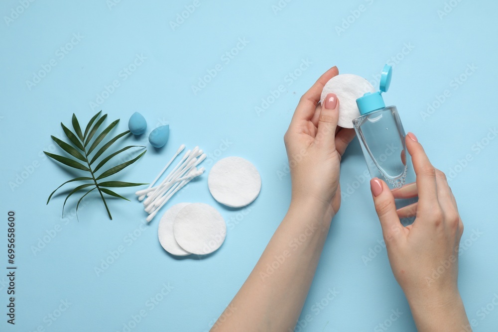 Woman using makeup remover, closeup. Sponges, cotton pads and buds on light blue background, top view - obrazy, fototapety, plakaty 