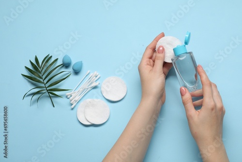 Woman using makeup remover, closeup. Sponges, cotton pads and buds on light blue background, top view