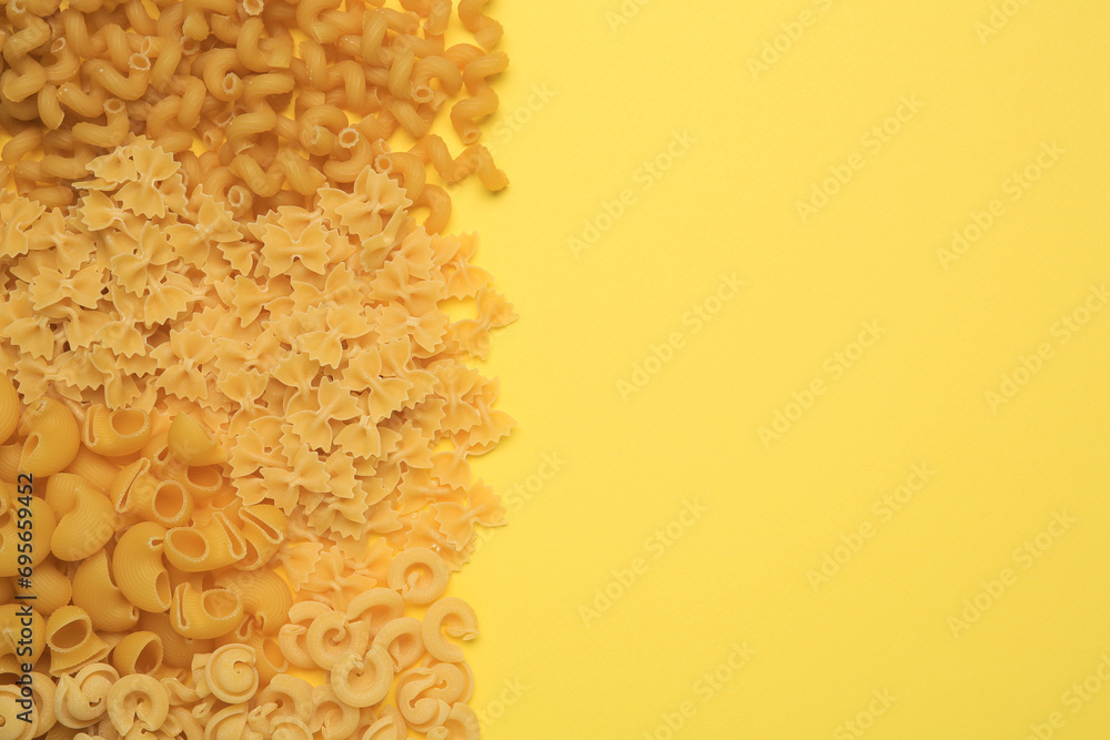 Obraz premium Different types of pasta on yellow background, flat lay. Space for text