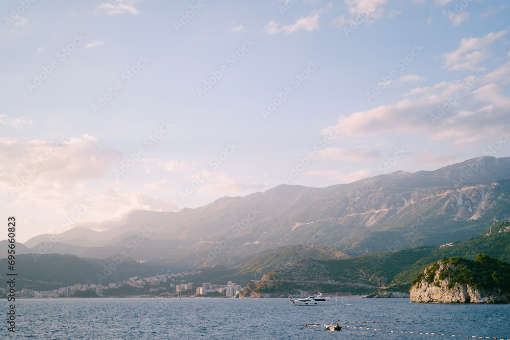 Motor yacht sails along the bay against the backdrop of a mountain range in bright sunlight
