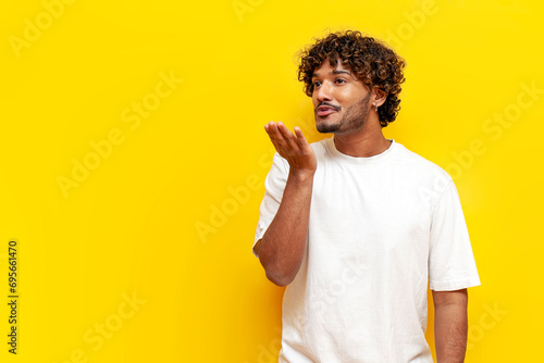 young indian guy blowing a kiss over yellow isolated background, south asian man in white t-shirt flirting